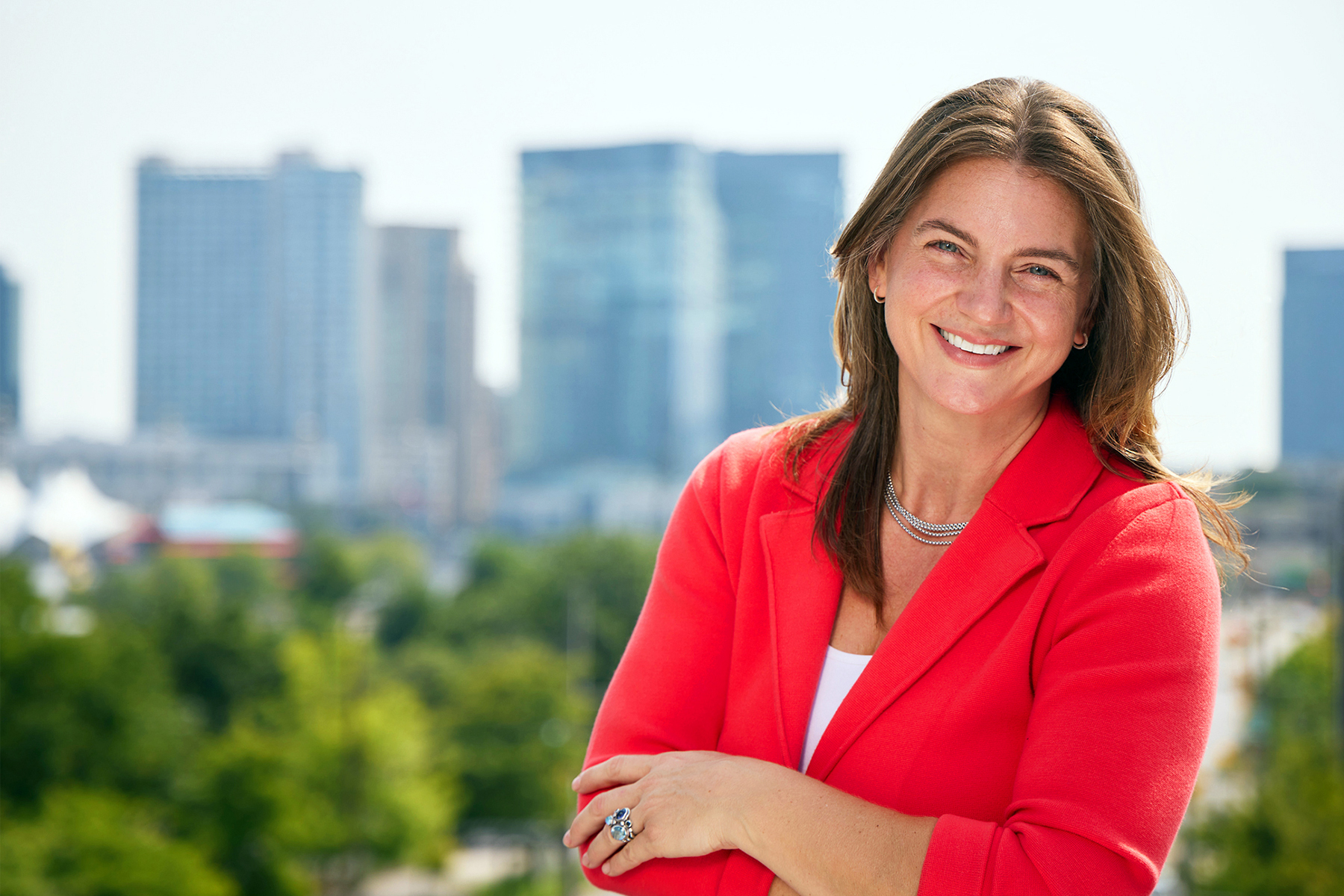 Headshot of Amanda Karfakis, CEO of the branding-digital-PR agency Vitamin standing on the rooftop of the agency's headquarters at 720 Light Street in Baltimore, Maryland, with the cityscape buildings and trees as a backdrop.